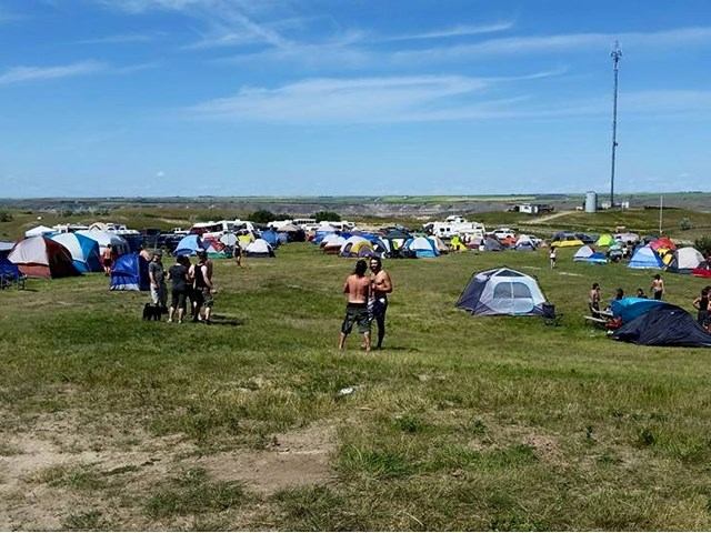 Festival campsite with colorful tents set up on grassy field under a clear blue sky.