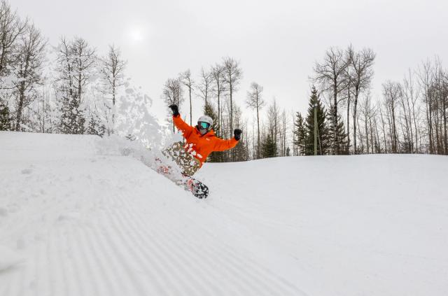 A snowboarder carves and sprays snow while snowboarding at Nitehawk Adventure Park in Grande Prairie