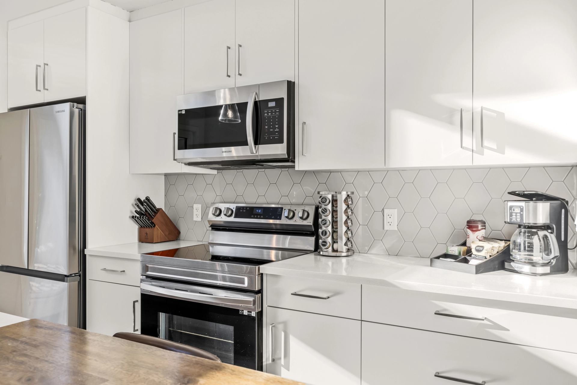 White kitchen with stainless steel appliances, hexagonal tile backsplash and coffee maker.
