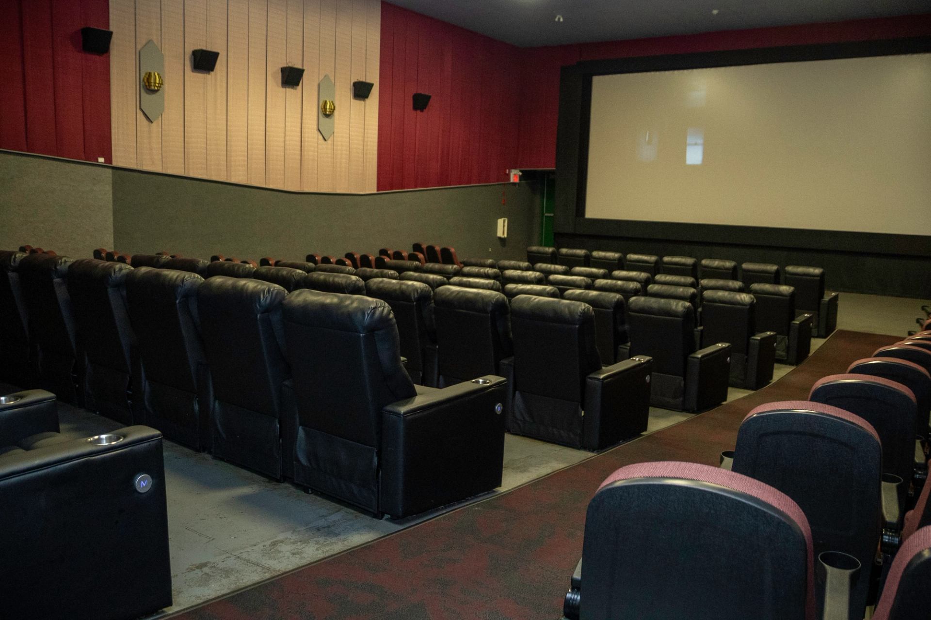 Empty cinema with black leather seats, red-gray walls, and large front screen.