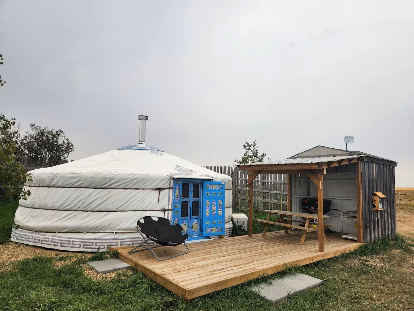 White yurt with a blue door beside a wooden deck and outdoor kitchen area.