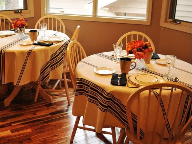 Dining table with striped tablecloths, place settings, flowers, and chairs inside a chalet.