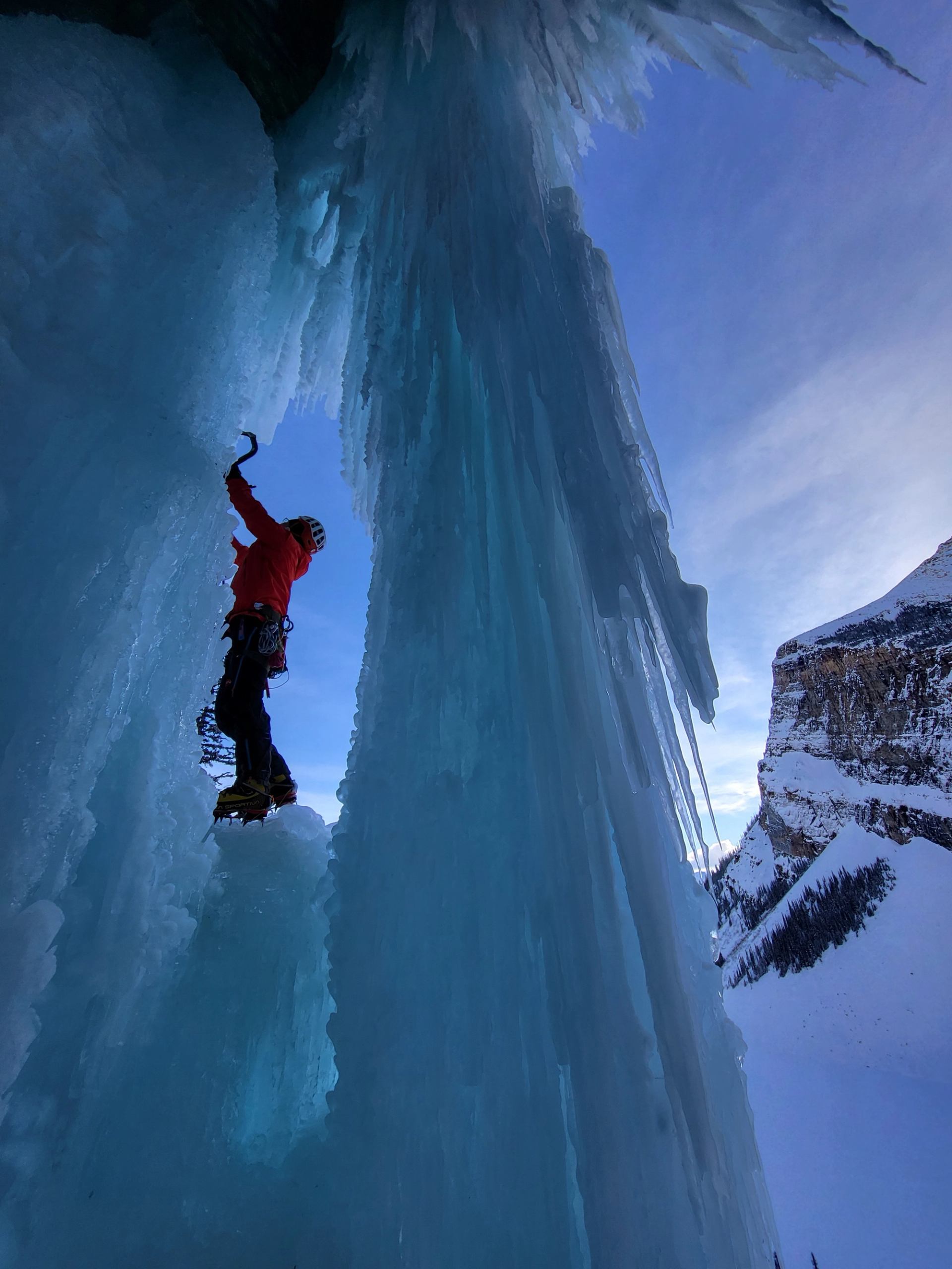 Ice climber scaling a vertical frozen wall under clear blue sky.
