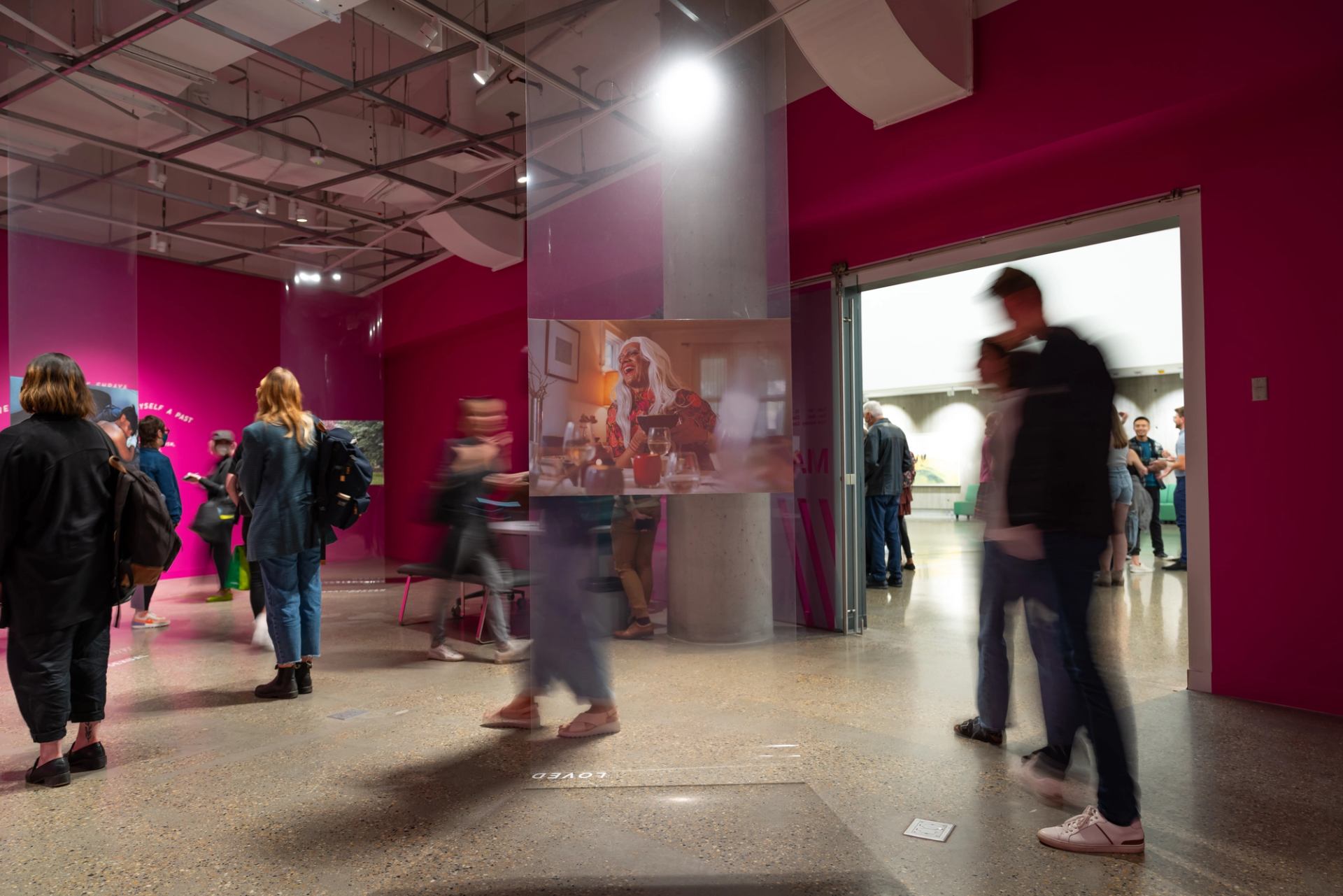 Visitors walking around photo installations in a gallery painted bright pink.
