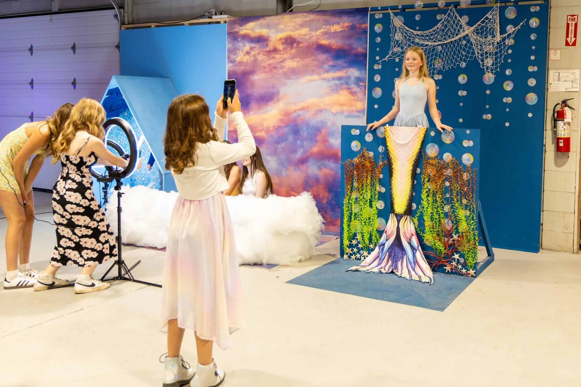 Children take photos at a mermaid-themed photo booth with colourful ocean backdrop.
