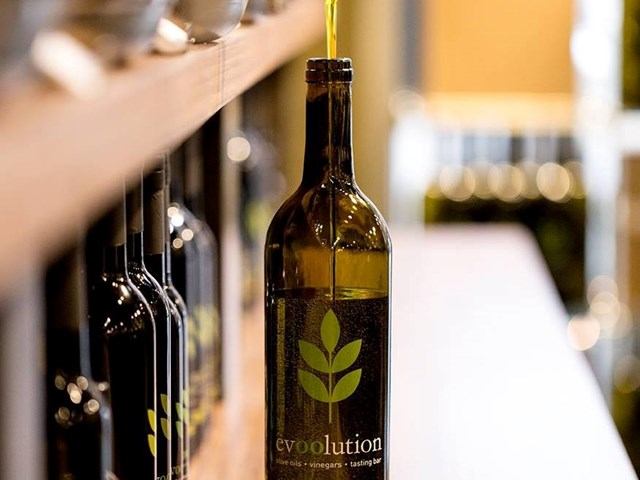 Olive oil bottle labeled “Evoolution” being filled, with others lined up in background.