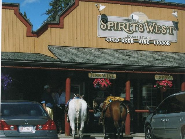 Spirits West Wine & Liquor storefront with horses on display and parked cars.