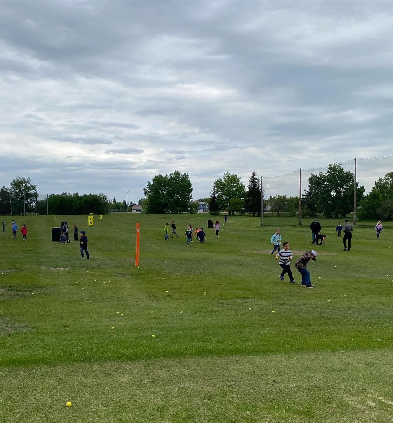 Golfers on manicured grass course near a tee marker, clubhouse in the distance.