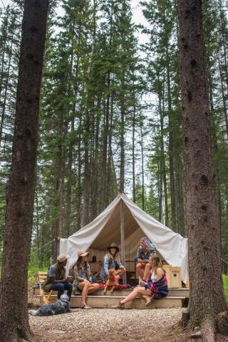 A group of friends sitting outside a comfort camping tent in the woods.