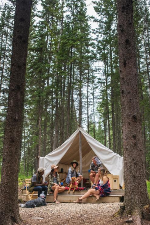 A group of friends sitting outside a comfort camping tent in the woods.