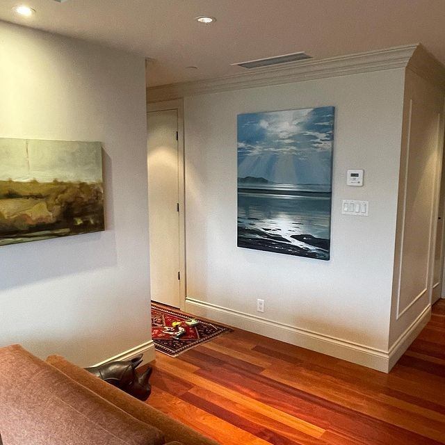 Art gallery interior with landscape paintings on walls, hardwood floor and area rug.