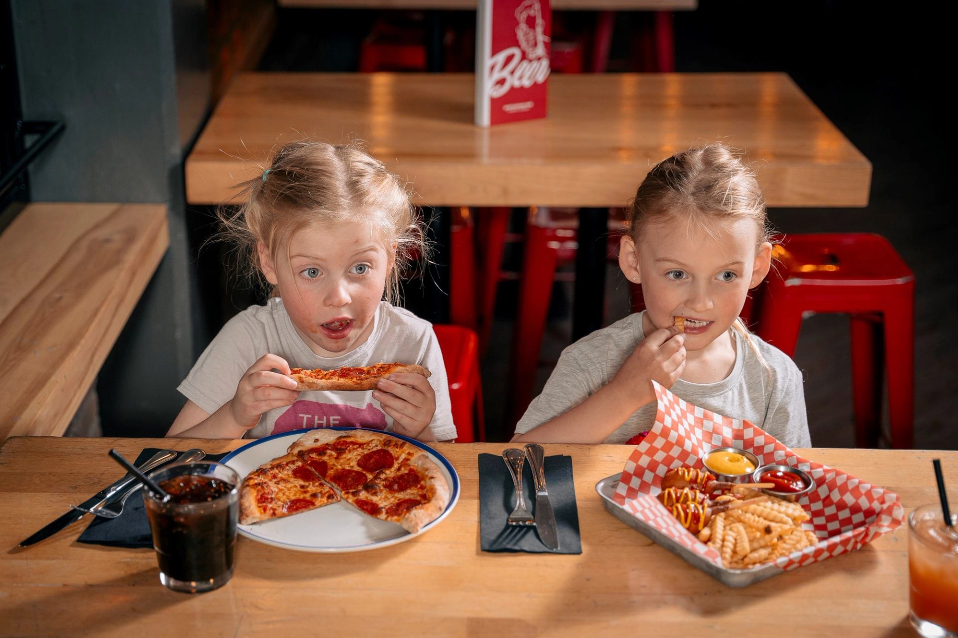 2 children eating a personal size pizza and mini corn dogs from kids menu.
