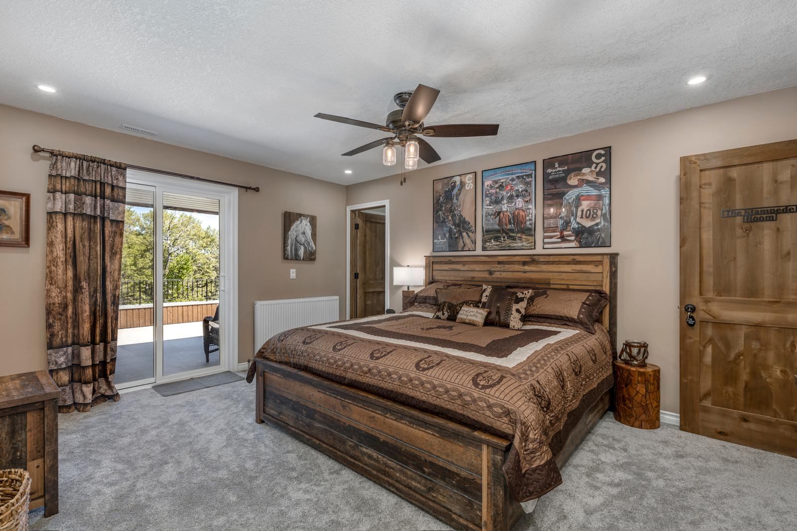 Rustic bedroom with wooden bed, horse artwork, ceiling fan and balcony doors.