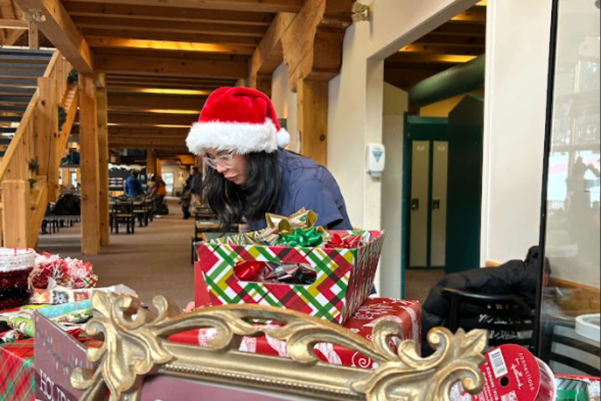 Holiday gift wrapping station with festive boxes and a person wearing a Santa hat.