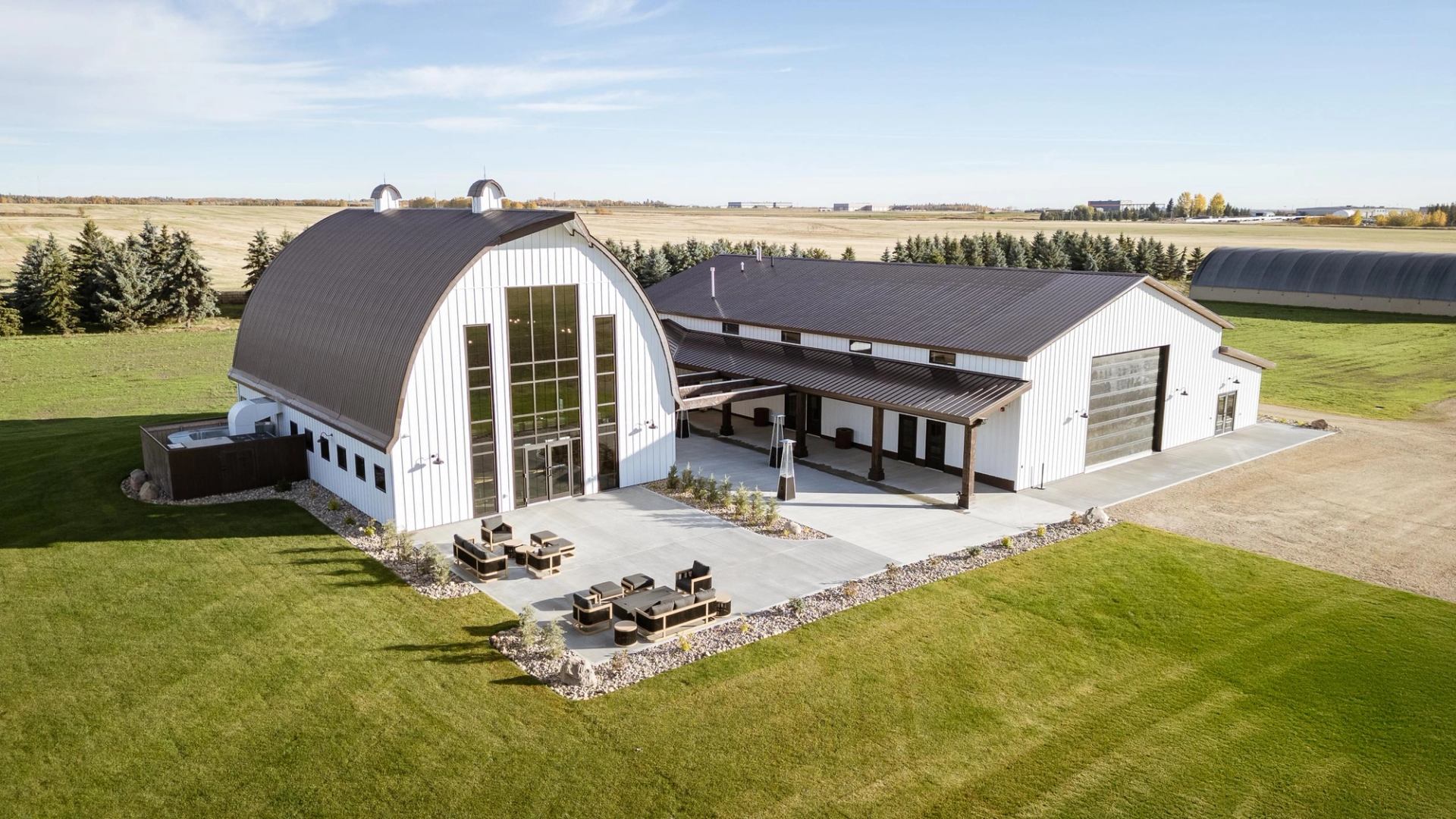 Aerial view of a modern barn‑style event venue with patio seating and wide open green space.
