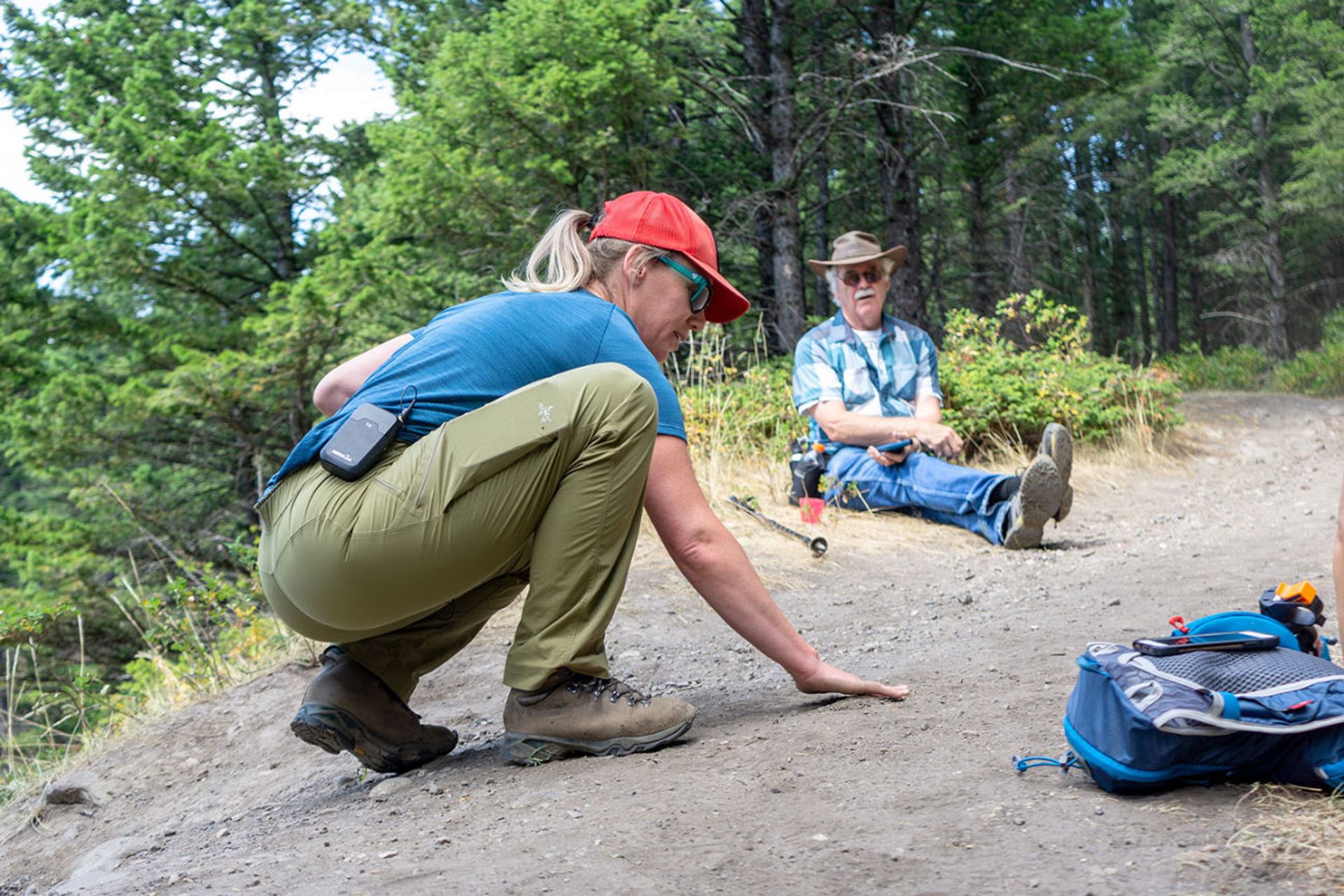 Guide kneeling near a seated hiker on a dirt path.