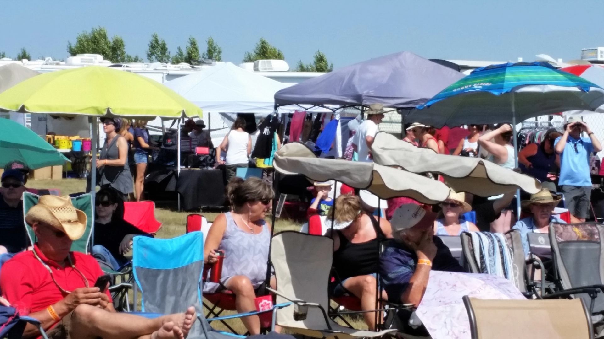 Outdoor music festival seating under colourful canopy tents, with attendees in rows.