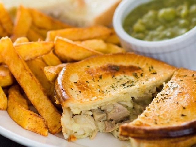 Plate of fries and sliced meat pie with ramekin of peas.
