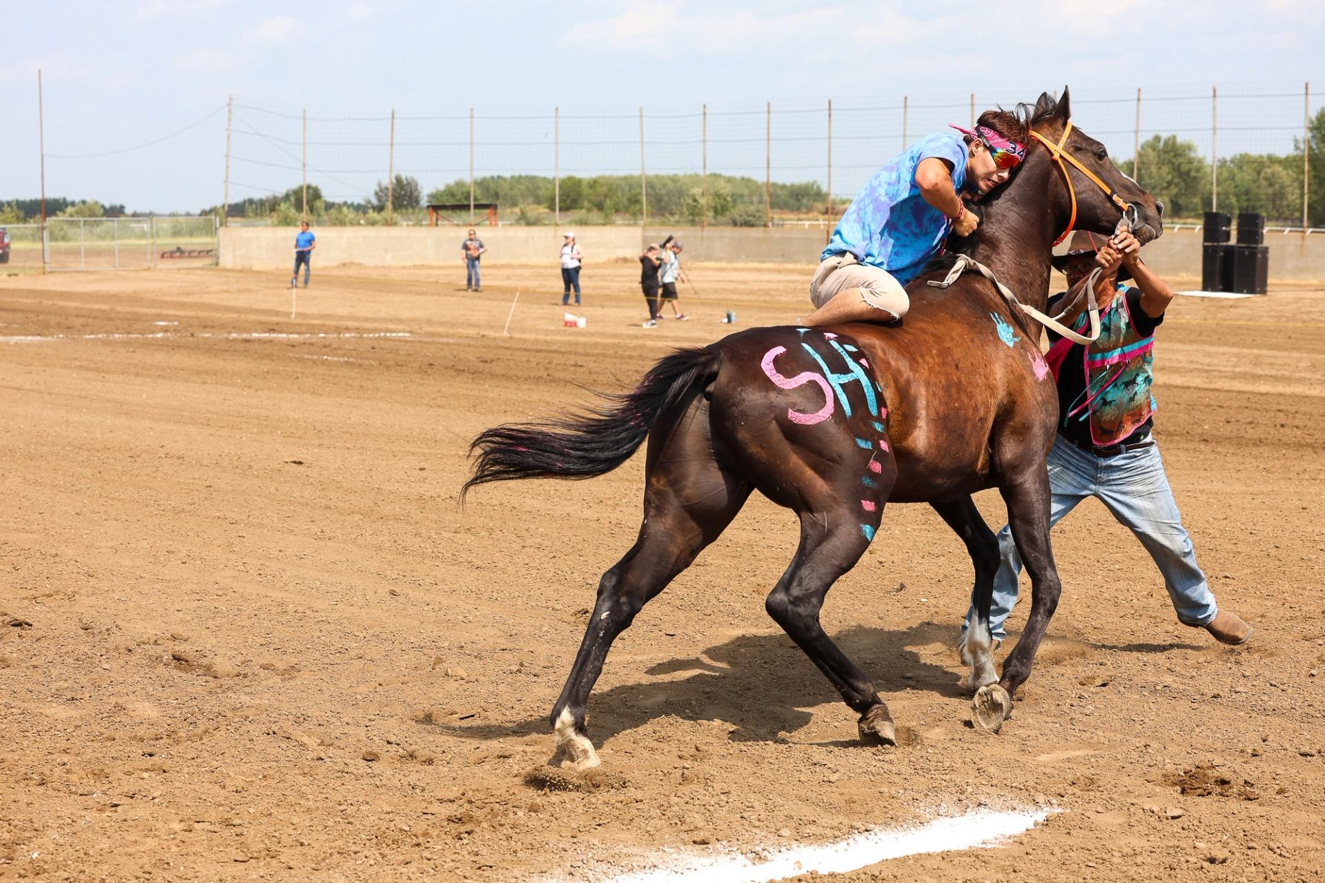 Horse and rider at rodeo relay, with painted horse and fencing in background.