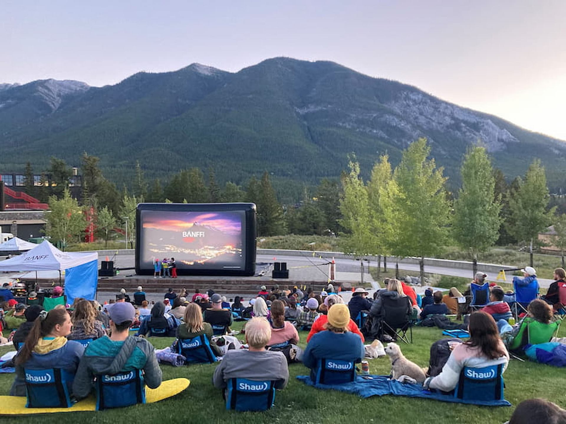 People sitting in lawn chairs watching a film on an outdoor screen.