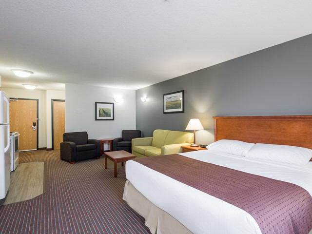 Hotel room with king bed, sofa seating area, kitchenette and framed wall art.