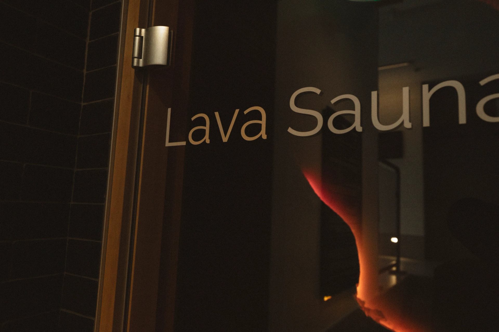 Glass door with Lava Sauna lettering and warm orange light reflection.