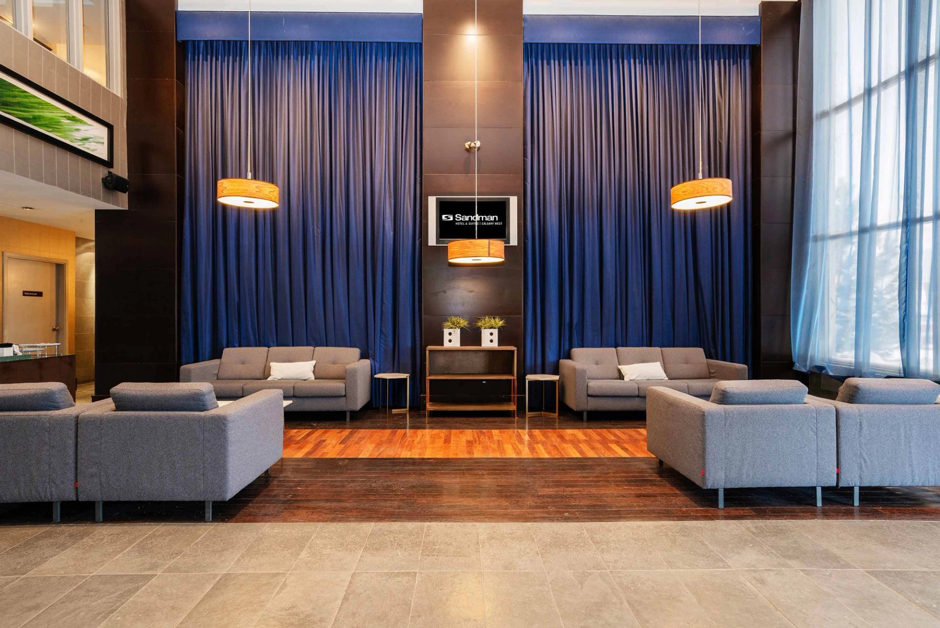 Hotel lobby with grey sofas, blue curtains, Sandman sign and hanging pendant lights.