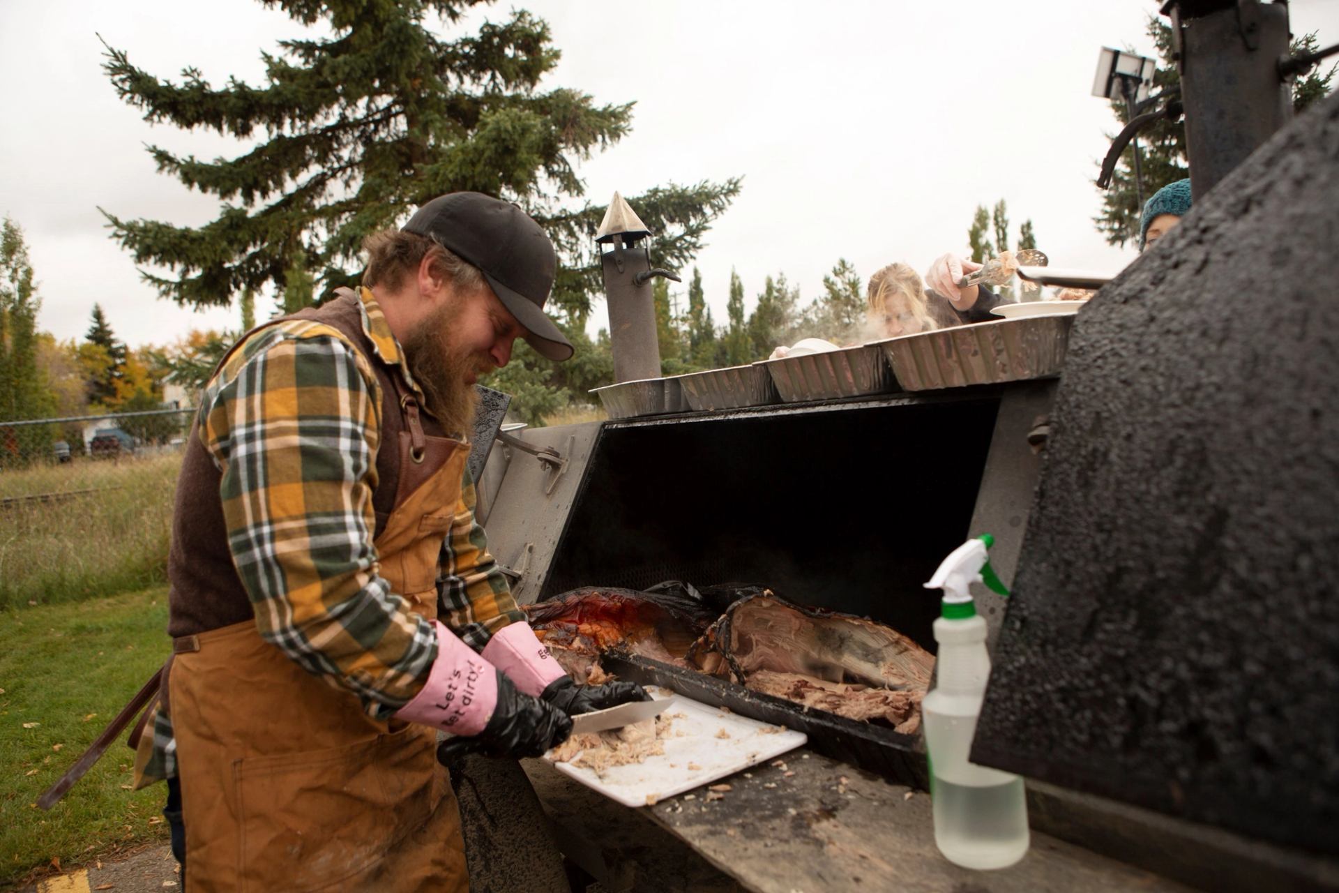 Person in flannel barbecuing meat at Flannel and Feast outdoor event.