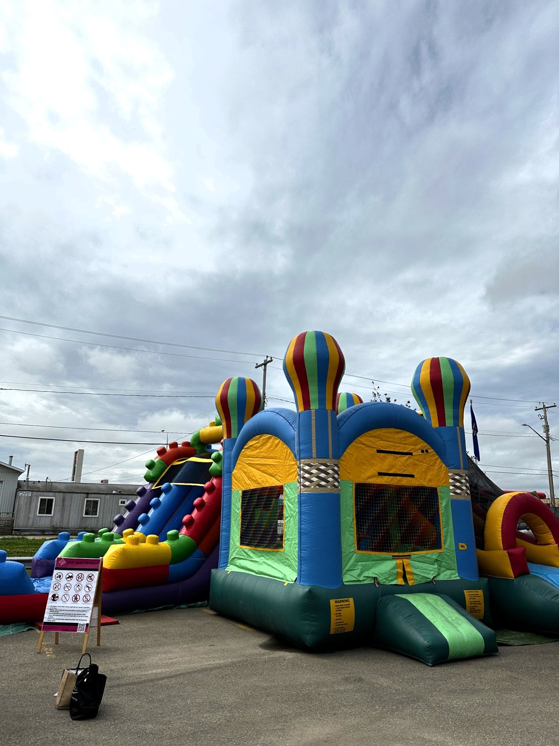Colourful inflatable bounce house and slide set up on asphalt under cloudy sky.