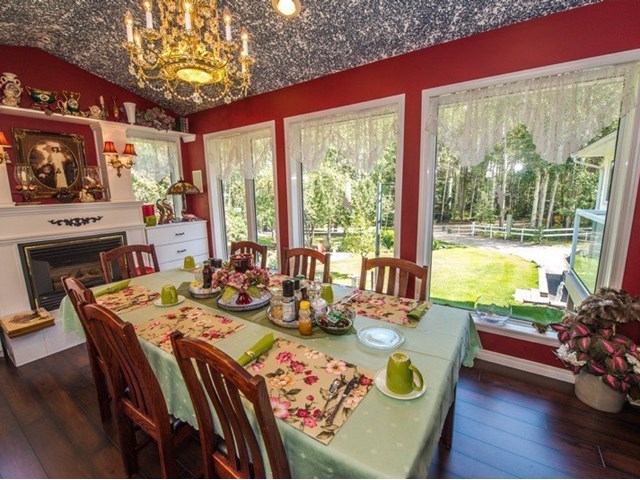 Dining room with red walls, large windows, and a table set for breakfast under a chandelier.