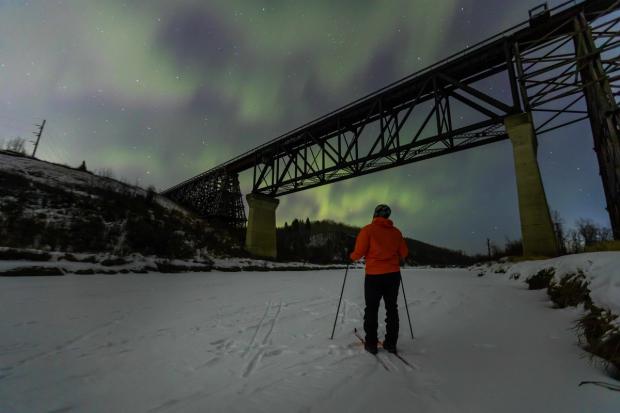 Person cross country skiing enjoying the Northern lights at Beaver River Trestle Bridge.