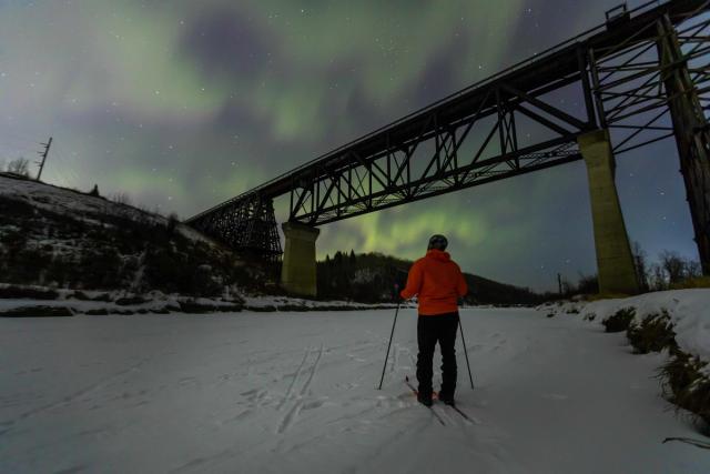 Person cross country skiing enjoying the Northern lights at Beaver River Trestle Bridge.