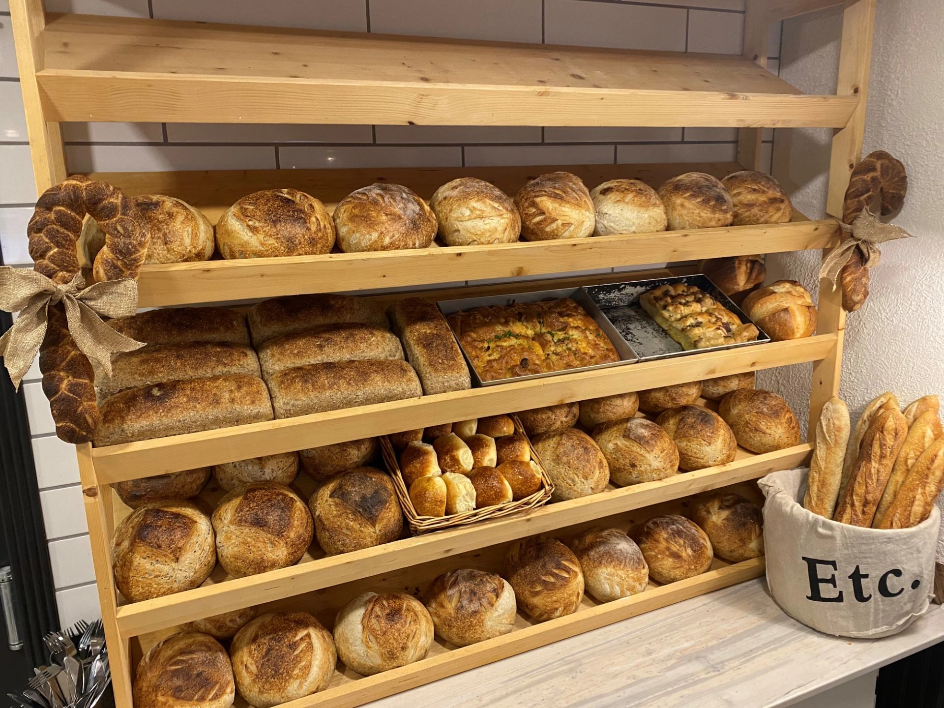 Bakery display shelves with loaves and rolls, including pretzels and flatbreads in trays.