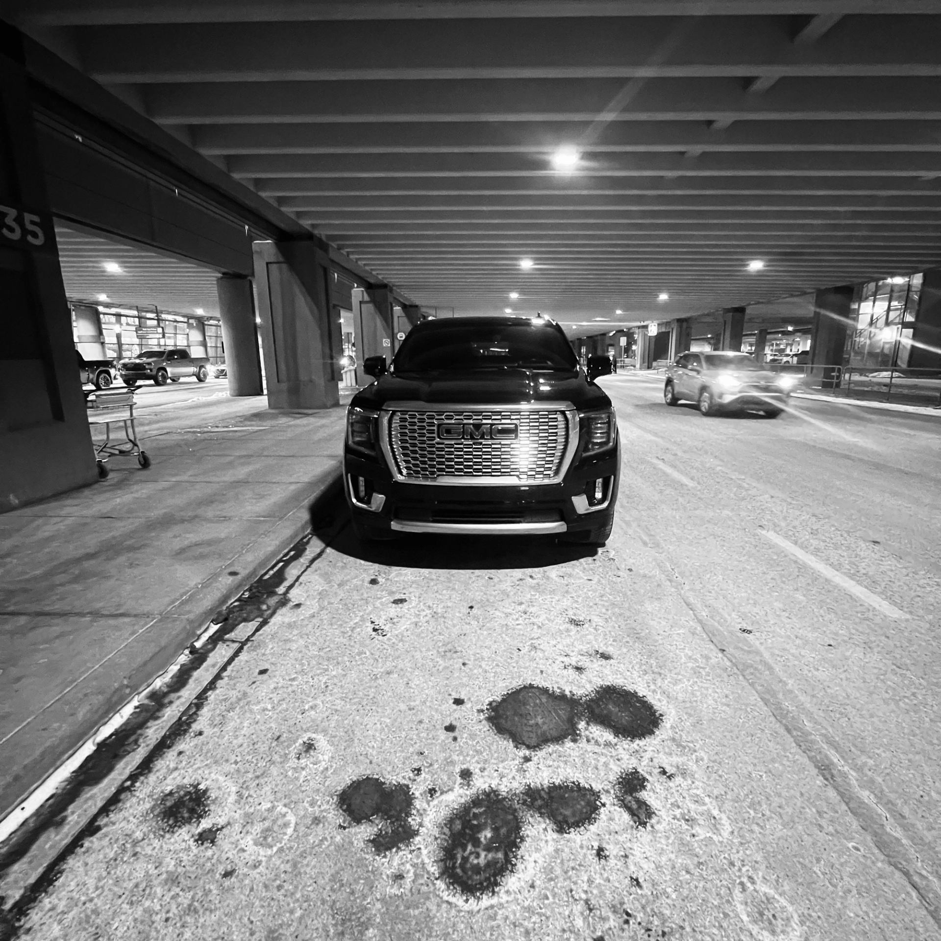 Black GMC SUV parked under overpass near curb, with passing car and shopping cart.