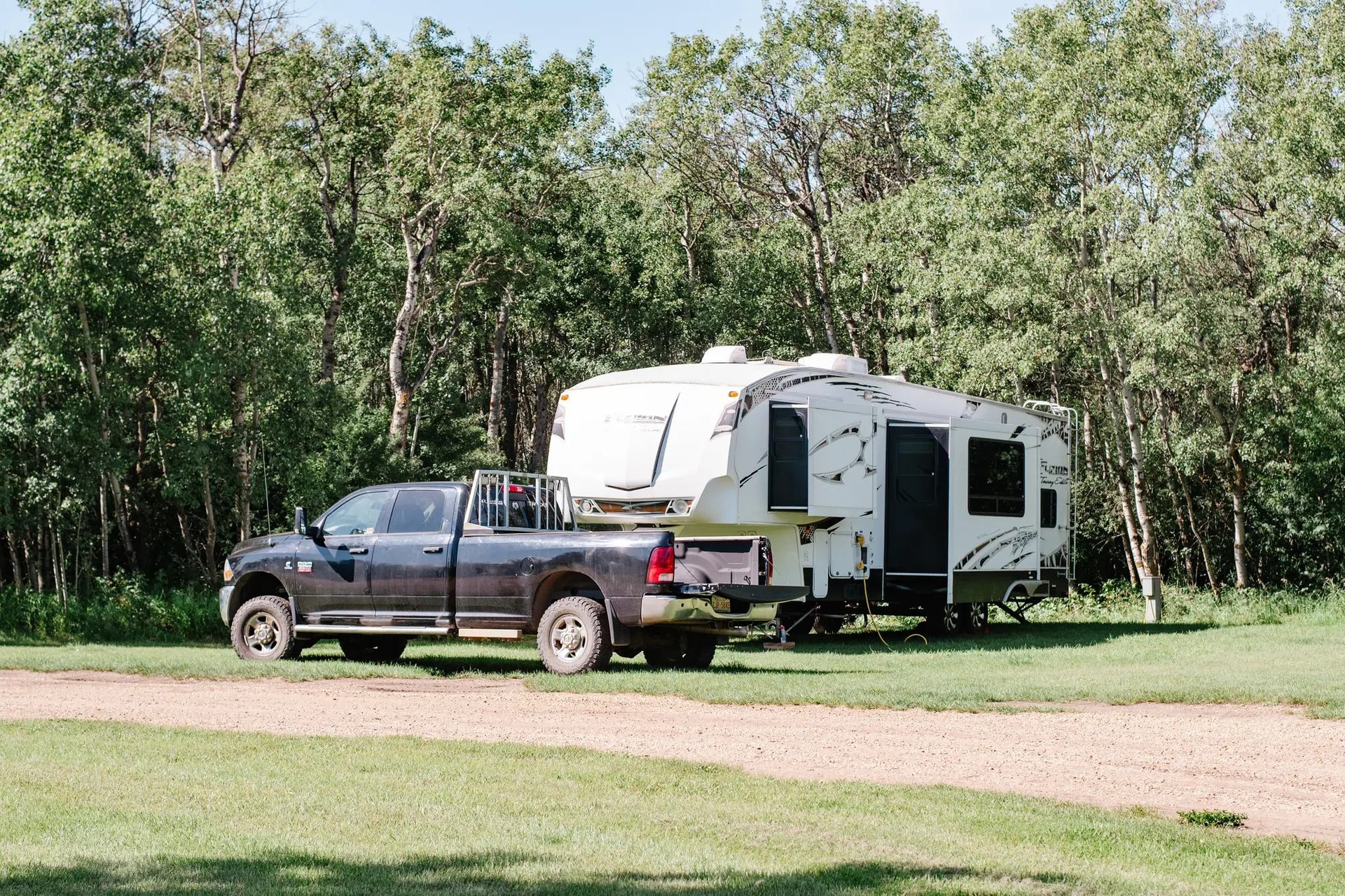 Pickup truck towing a large fifth-wheel trailer parked on grass near trees.