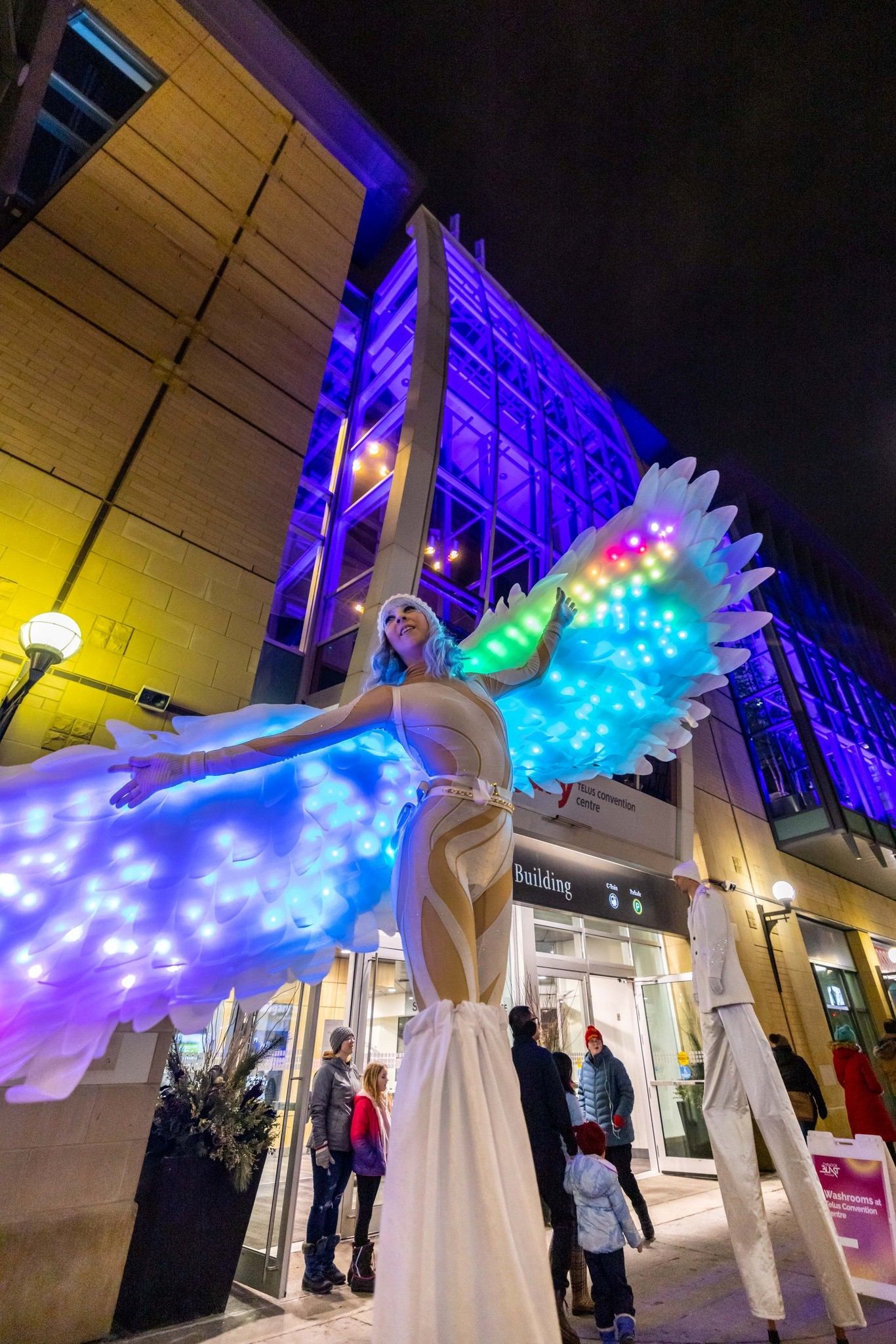 Tall stilt walker in glowing wings greets downtown visitors