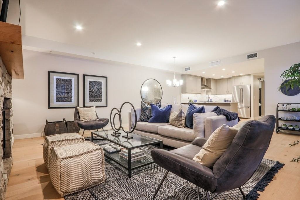 Modern living room with gray sofas, glass coffee table, and open kitchen in the background.
