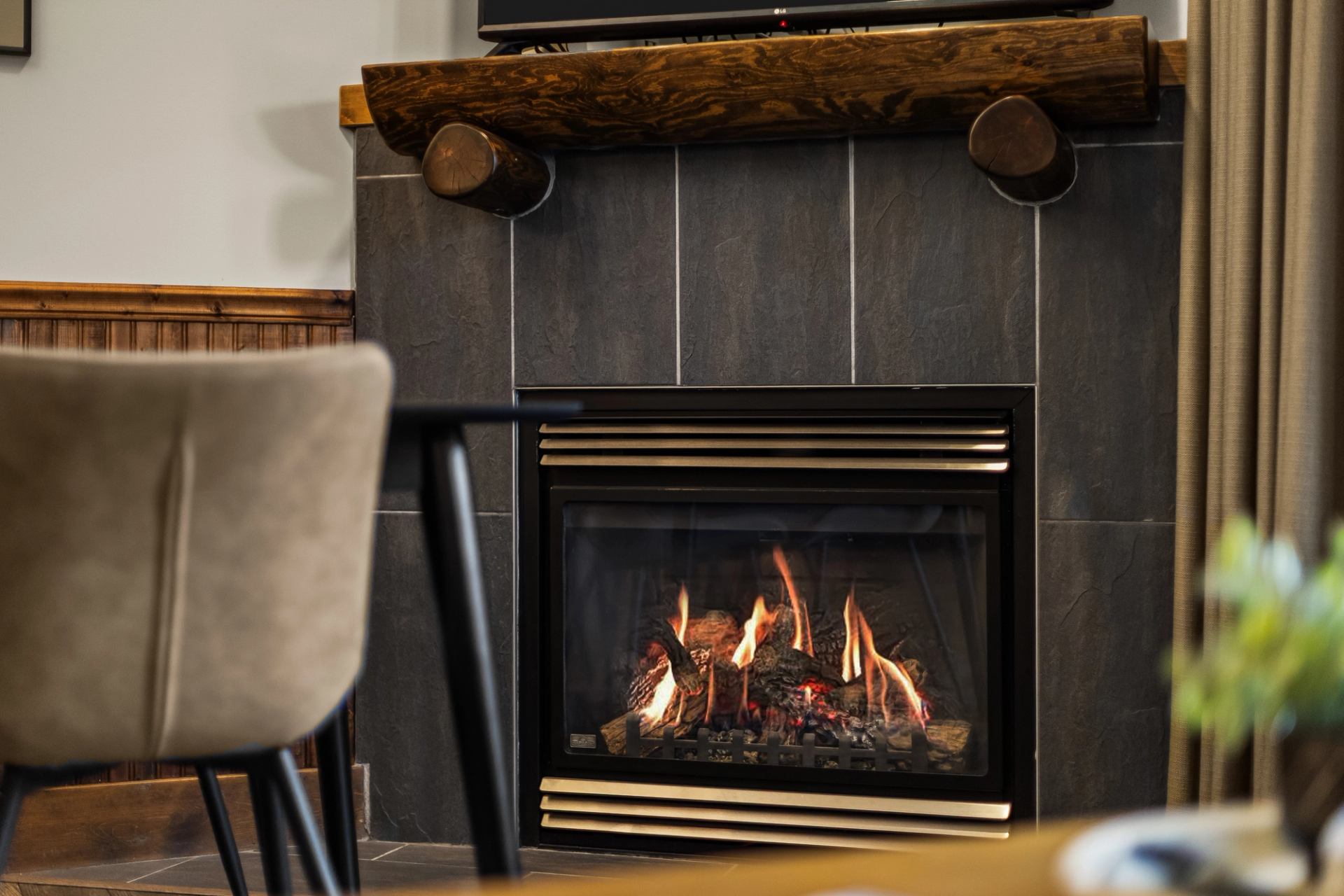 Lit fireplace framed by dark tiles and a rustic wooden mantel.