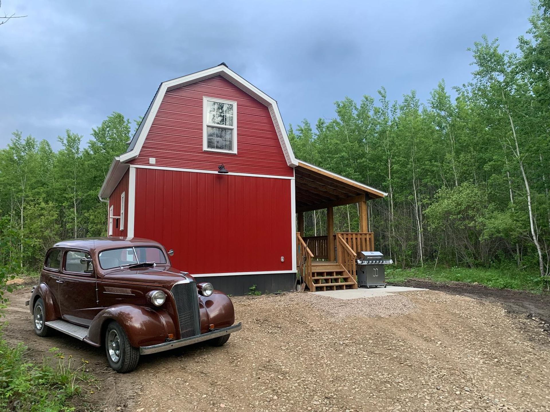 Red cabin in forest with vintage car at Wildly Eweneek Cabins.