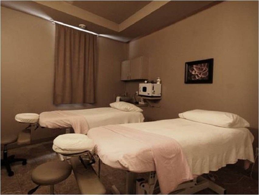 Treatment room with three massage beds, massage chairs, and a wall mirror.