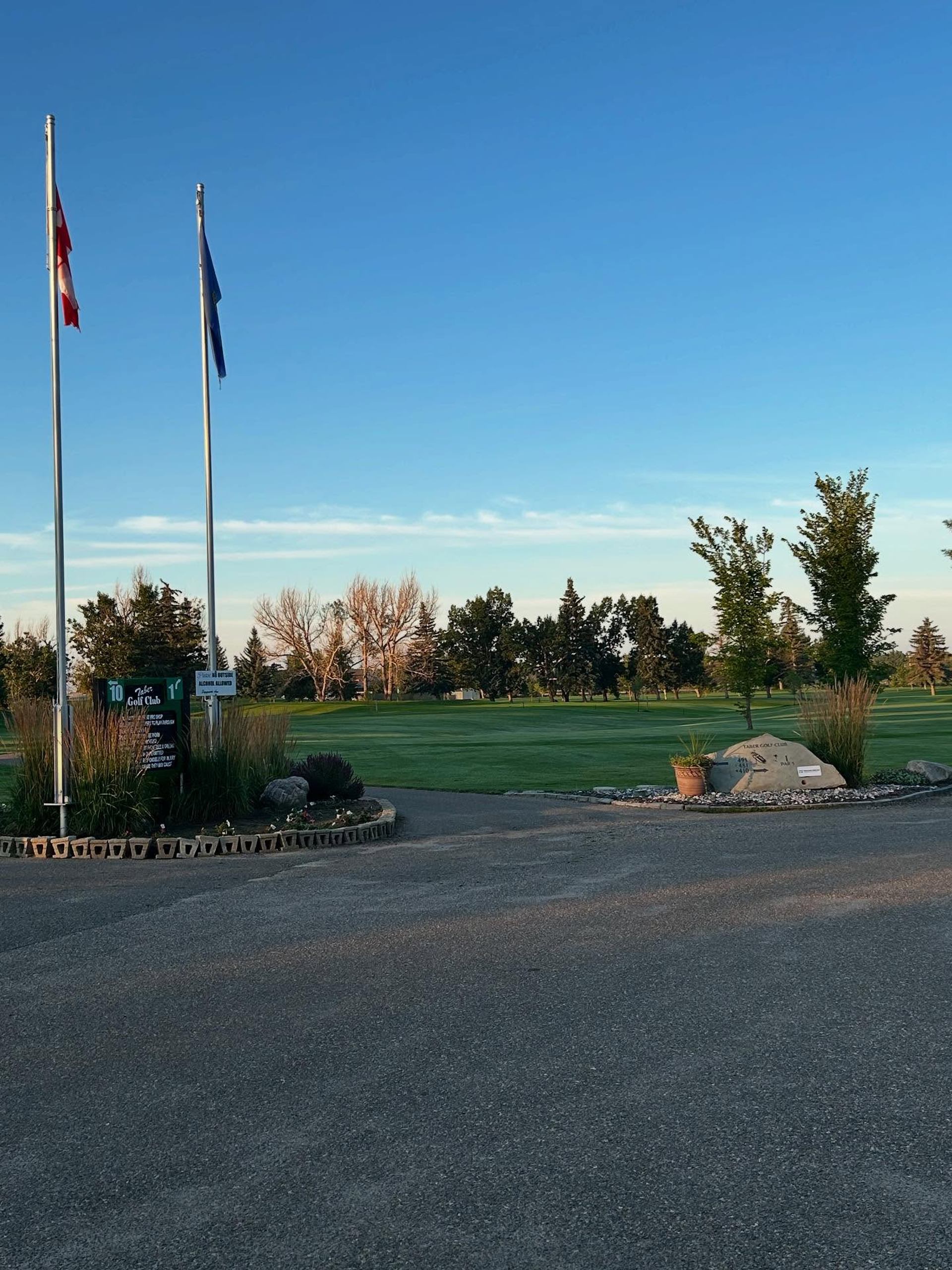 Entrance area of Taber Golf Club with flags, landscaping, and the course beyond.