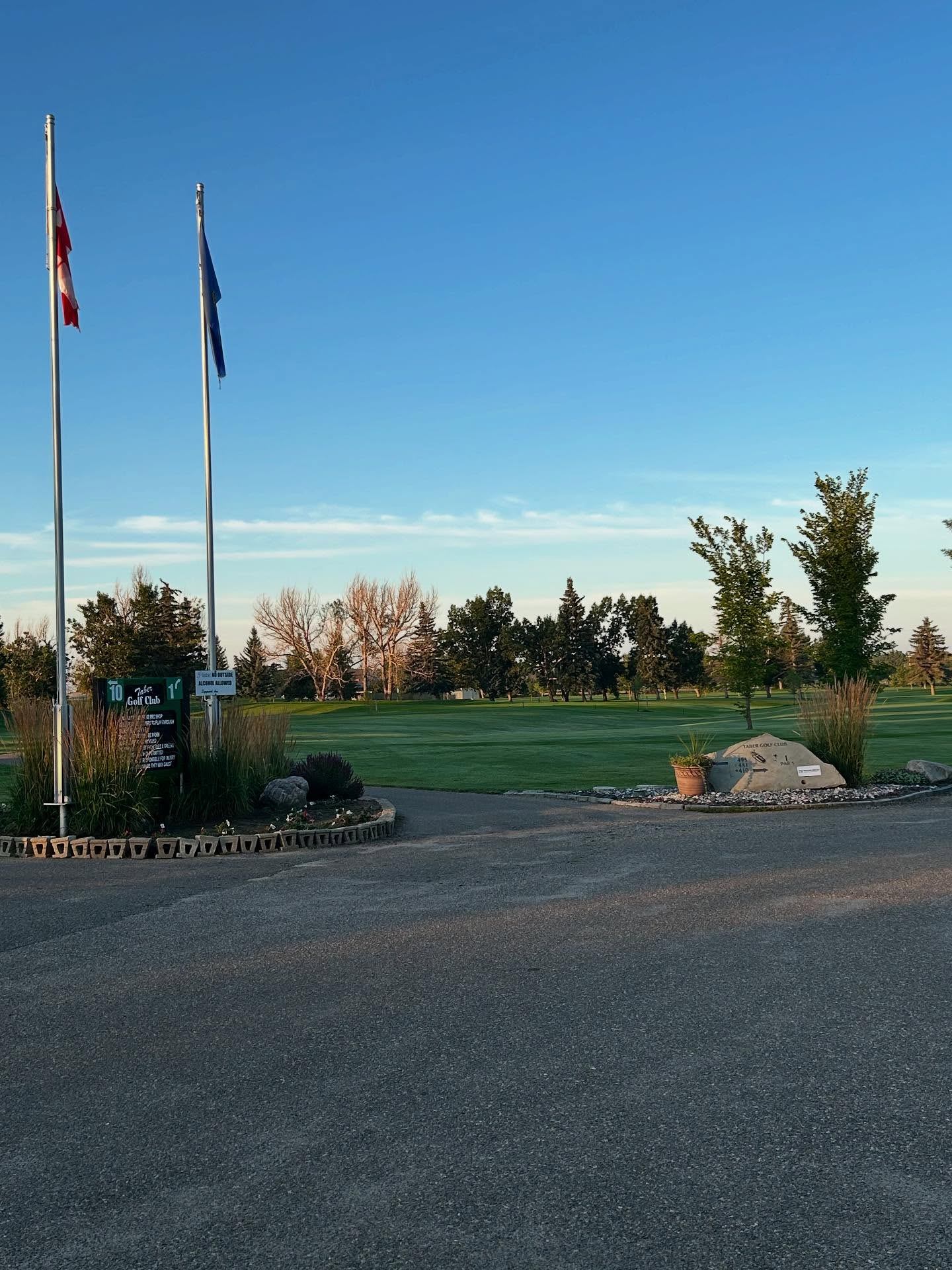 Entrance area of Taber Golf Club with flags, landscaping, and the course beyond.