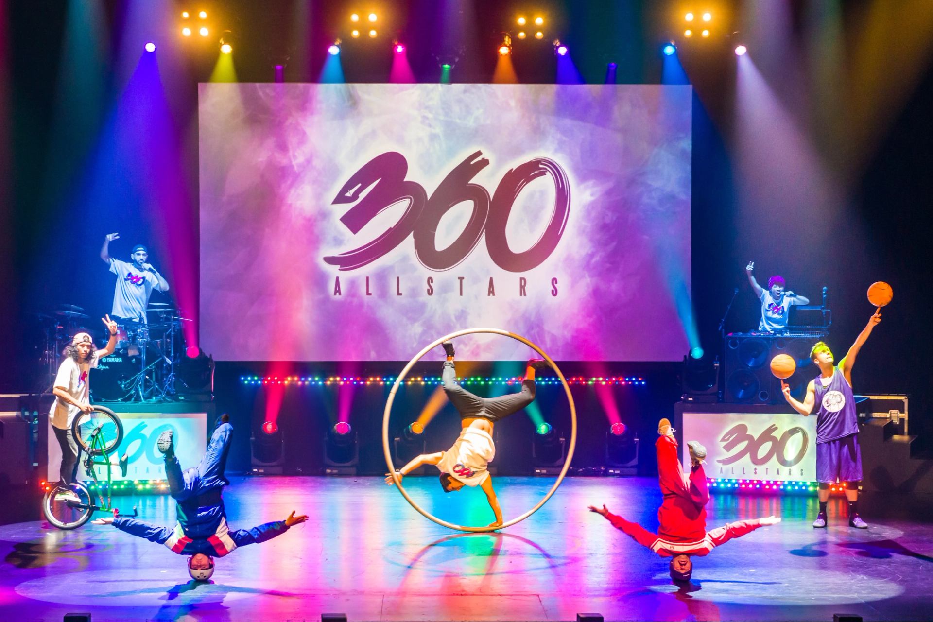 Stage performers breakdance, spin in a hoop and juggle basketballs under colourful lights.