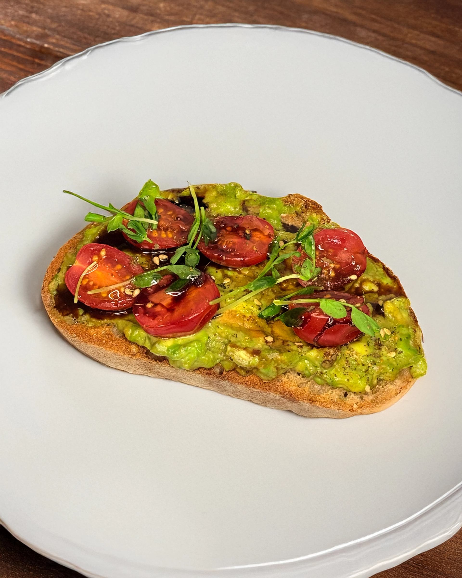 Avocado toast with cherry tomatoes and microgreens on a white plate.