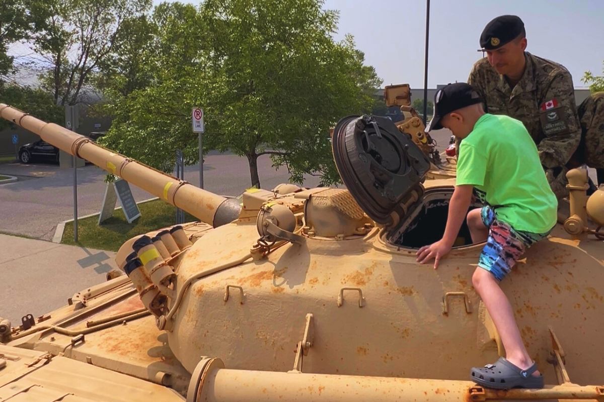 Tank vehicle with soldier and child standing beside the turret outdoors at a park.