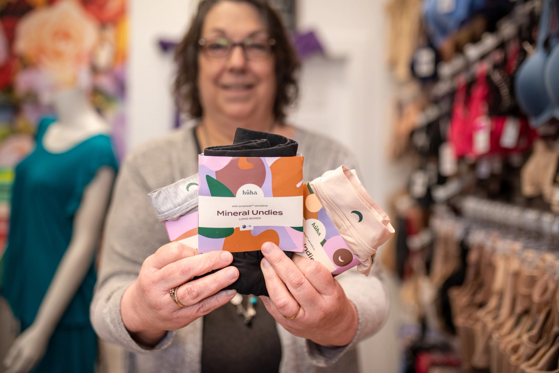 Person holds húha Mineral Undies packages in lingerie store, racks and mannequin behind.
