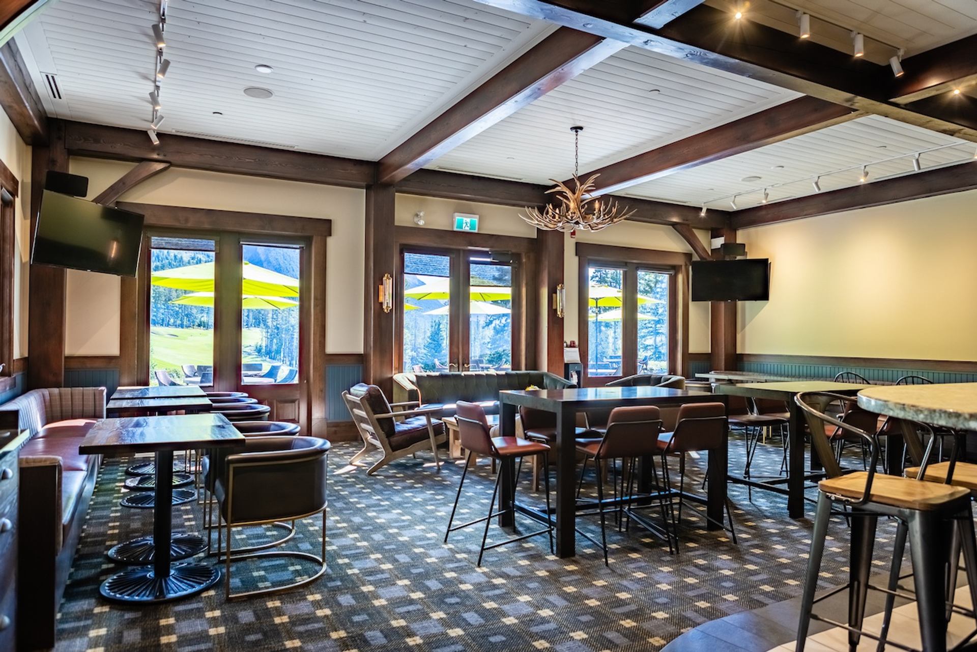 Indoor lounge with tables, bar seating, and windows facing the patio