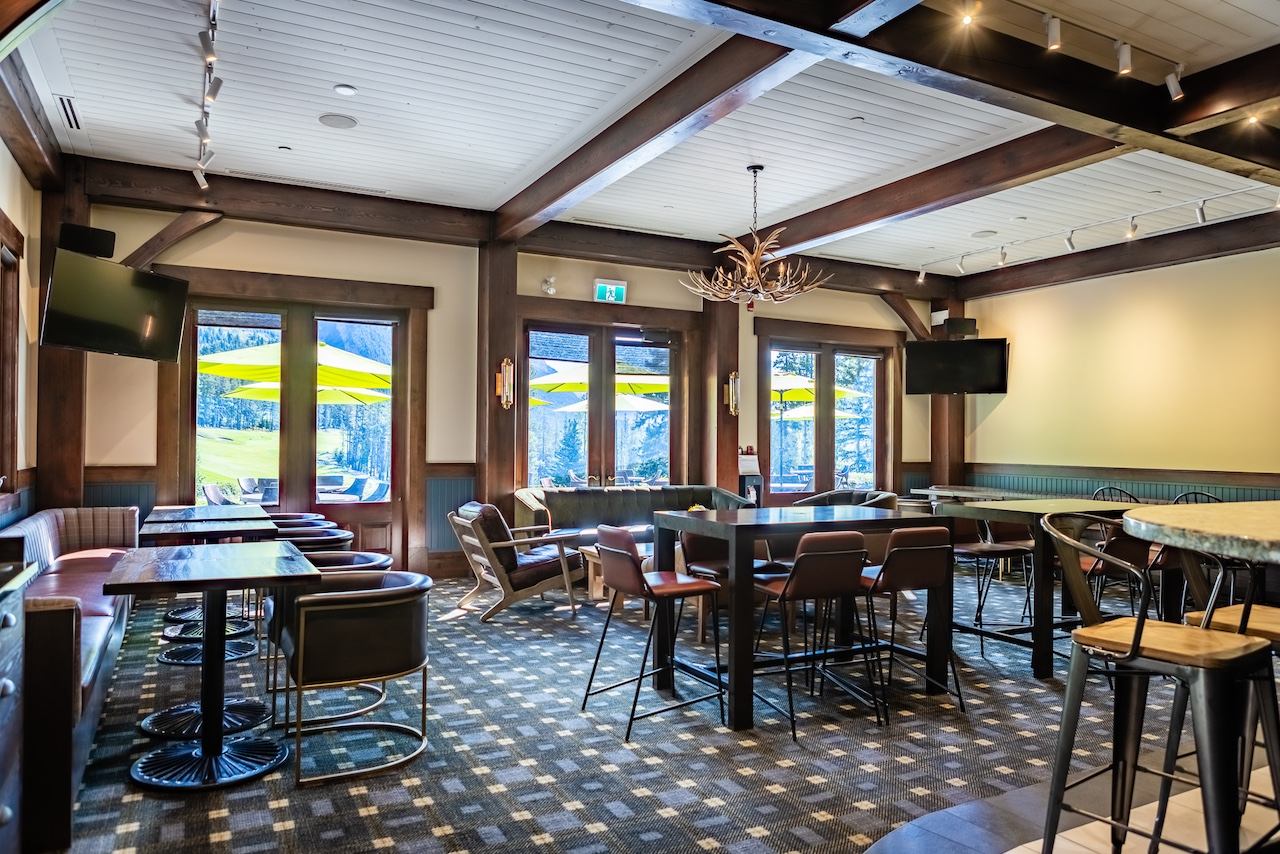 Indoor lounge with tables, bar seating, and windows facing the patio