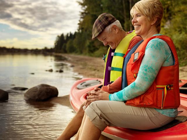 Older couple sitting on a Kayak with their feet in the water on the shore of Cold Lake.