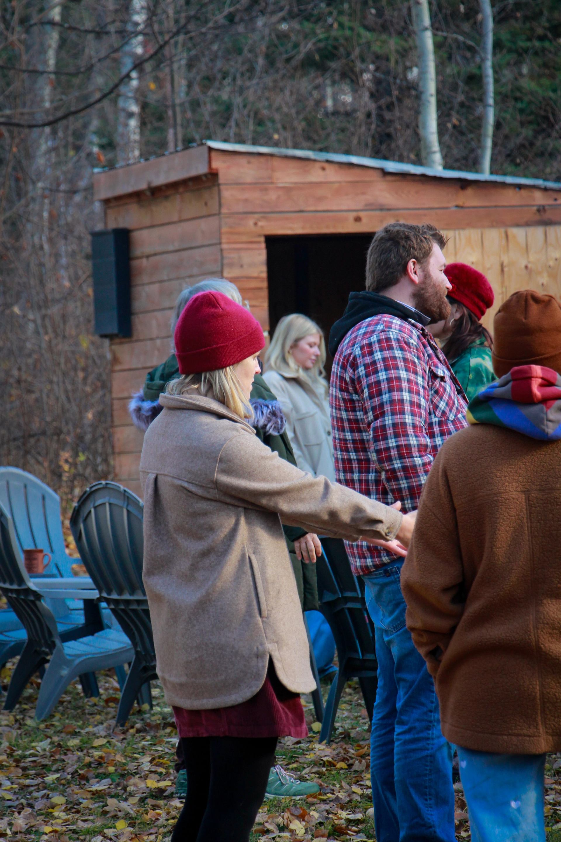 Group gathering outdoors near a wooden shed, preparing for a forest walk.